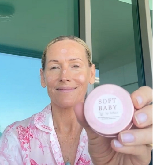 Woman holding a pink jar labeled 'Soft Baby' outdoors