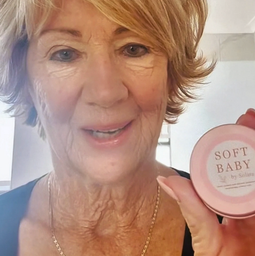Woman holding a pink container labeled 'Soft Baby' in front of her face.
